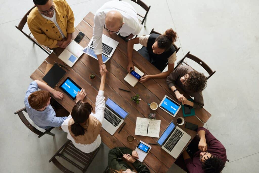business-meeting-around-a-table-2-people-shaking-hands-laptops-phones-on-table