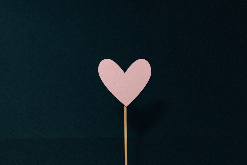 a paper pink heart stuck onto a stick on a black background