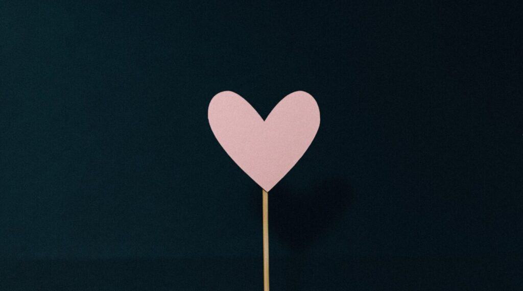 a paper pink heart stuck onto a stick on a black background