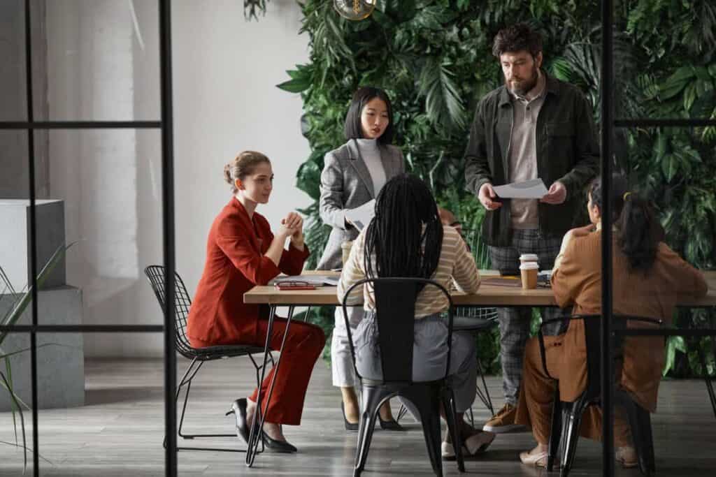 raphic full length portrait of diverse group of business people meeting at table in modern office interior, copy space